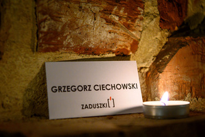 Koncert: Zaduszki - Element scenografii - etykieta z napisem Grzegorz Ciechowski oświetlona świeczką.