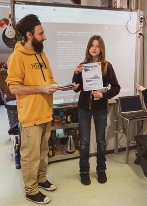 Artystyczne Ferie - tydzień II - Na fotografii uwieczniono grupę uczestników – dzieci, młodzież oraz dorosłych – zaangażowanych w warsztaty tworzenia Artbooków. Widoczne są różnorodne narzędzia, w tym prasa drukarska, z których korzystają pod czujnym okiem prowadzących.