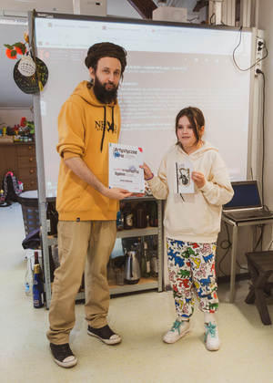 Artystyczne Ferie - tydzień II - Na fotografii uwieczniono grupę uczestników – dzieci, młodzież oraz dorosłych – zaangażowanych w warsztaty tworzenia Artbooków. Widoczne są różnorodne narzędzia, w tym prasa drukarska, z których korzystają pod czujnym okiem prowadzących.