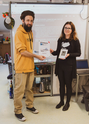 Artystyczne Ferie - tydzień II - Na fotografii uwieczniono grupę uczestników – dzieci, młodzież oraz dorosłych – zaangażowanych w warsztaty tworzenia Artbooków. Widoczne są różnorodne narzędzia, w tym prasa drukarska, z których korzystają pod czujnym okiem prowadzących.