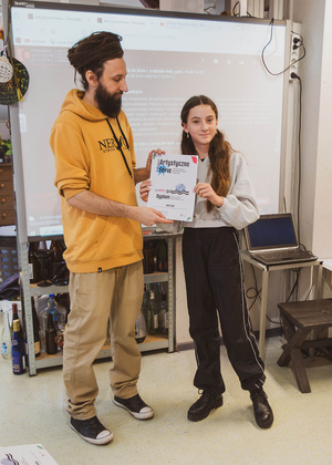 Artystyczne Ferie - tydzień II - Na fotografii uwieczniono grupę uczestników – dzieci, młodzież oraz dorosłych – zaangażowanych w warsztaty tworzenia Artbooków. Widoczne są różnorodne narzędzia, w tym prasa drukarska, z których korzystają pod czujnym okiem prowadzących.