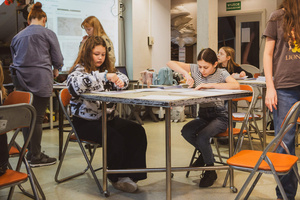 Artystyczne Ferie - tydzień II - Na fotografii uwieczniono grupę uczestników – dzieci, młodzież oraz dorosłych – zaangażowanych w warsztaty tworzenia Artbooków. Widoczne są różnorodne narzędzia, w tym prasa drukarska, z których korzystają pod czujnym okiem prowadzących.