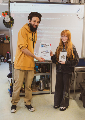 Artystyczne Ferie - tydzień II - Na fotografii uwieczniono grupę uczestników – dzieci, młodzież oraz dorosłych – zaangażowanych w warsztaty tworzenia Artbooków. Widoczne są różnorodne narzędzia, w tym prasa drukarska, z których korzystają pod czujnym okiem prowadzących.