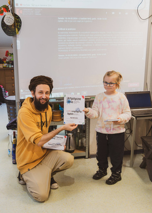 Artystyczne Ferie - tydzień II - Na fotografii uwieczniono grupę uczestników – dzieci, młodzież oraz dorosłych – zaangażowanych w warsztaty tworzenia Artbooków. Widoczne są różnorodne narzędzia, w tym prasa drukarska, z których korzystają pod czujnym okiem prowadzących.