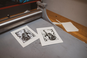 Artystyczne Ferie - tydzień II - Na fotografii uwieczniono grupę uczestników – dzieci, młodzież oraz dorosłych – zaangażowanych w warsztaty tworzenia Artbooków. Widoczne są różnorodne narzędzia, w tym prasa drukarska, z których korzystają pod czujnym okiem prowadzących.