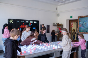 Naukowe Ferie w Pasażu Odkryć - Na zdjęciu przedstawieni są uczestnicy – dzieci i młodzież – zaangażowani w aktywności edukacyjne w różnych pracowniach naukowych, takich jak chemiczna, stolarska, planetarium oraz informatyczna. Widoczne są sceny, gdzie uczą się i przeprowadzają eksperymenty pod nadzorem instruktorów.