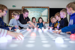 Naukowe Ferie w Pasażu Odkryć - Na zdjęciu przedstawieni są uczestnicy – dzieci i młodzież – zaangażowani w aktywności edukacyjne w różnych pracowniach naukowych, takich jak chemiczna, stolarska, planetarium oraz informatyczna. Widoczne są sceny, gdzie uczą się i przeprowadzają eksperymenty pod nadzorem instruktorów.