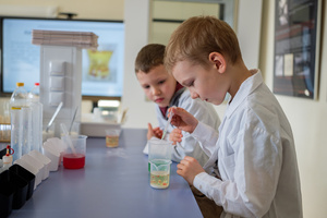 Naukowe Ferie w Pasażu Odkryć - Na zdjęciu przedstawieni są uczestnicy – dzieci i młodzież – zaangażowani w aktywności edukacyjne w różnych pracowniach naukowych, takich jak chemiczna, stolarska, planetarium oraz informatyczna. Widoczne są sceny, gdzie uczą się i przeprowadzają eksperymenty pod nadzorem instruktorów.