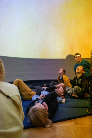 Naukowe Ferie w Pasażu Odkryć - Na zdjęciu przedstawieni są uczestnicy – dzieci i młodzież – zaangażowani w aktywności edukacyjne w różnych pracowniach naukowych, takich jak chemiczna, stolarska, planetarium oraz informatyczna. Widoczne są sceny, gdzie uczą się i przeprowadzają eksperymenty pod nadzorem instruktorów.