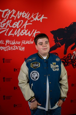 38. TNF - Dzień 6 (5.06.2024) - Odtwórca głównej roli w filmie "Za duży na bajki 2" Maciej Karaś na tle ścianki festiwalowej w Marzeniu