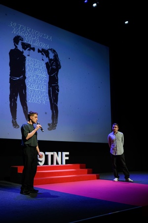 39. TNF: Dzień 4 (2.06.2025) - Na scenie Marzenia Damian Kocur, reżyser filmu "Pod wulkanem" zapraszający widzów na projekcję. W tle Kuba Armata