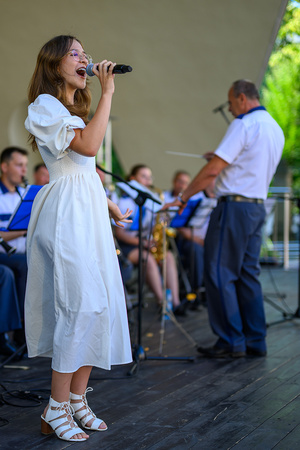 Koncert Polskiej Muzyki Rozrywkowej - Orkiestra Dęta Grupy Azoty S.A. i soliści - Na amfiteatralnej scenie na pierwszym planie śpiewająca solistka Aleksandra Wojnarska i dyrygent Jacek Skrzelowski