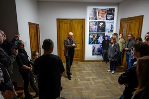 Wystawa: w cyklu Wernisaże Dzień po Dniu - W głębi Tomasz Sobczak podczas przemowy, po prawej plakaty wystawi autorzy.